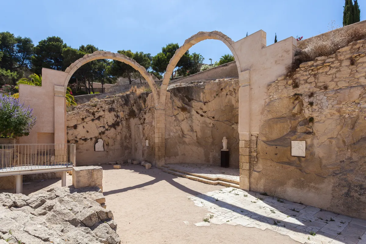 Two tall stone arches among pale ruins inside Santa Bárbara Castle, with pine trees behind
