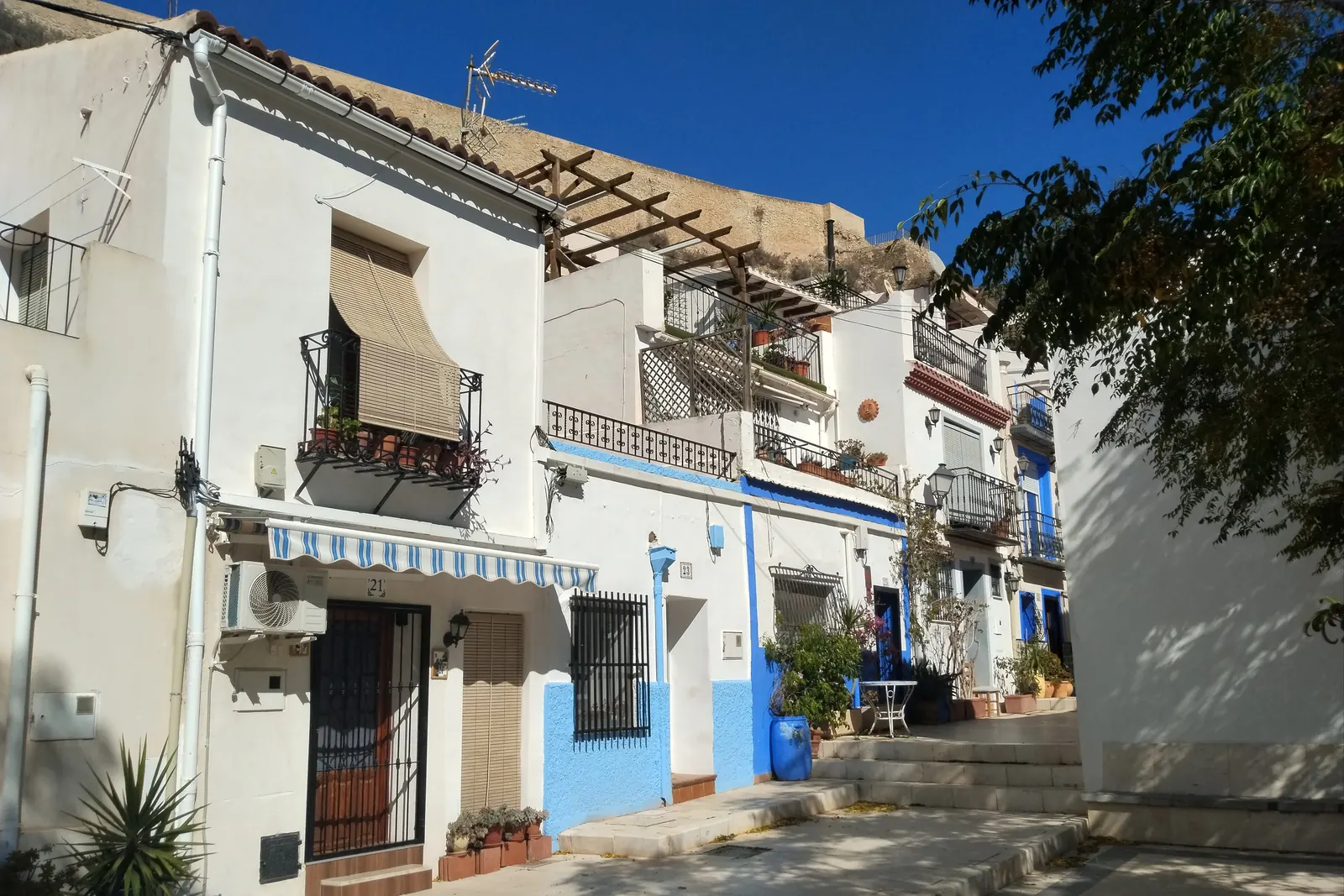 White houses with blue base-coats and green shutters on Calle San Antonio in Santa Cruz, with the rock of the castle hill above; a general photograph of the quarter